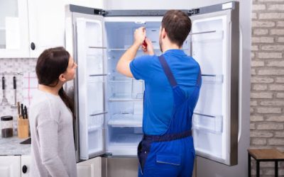 Woman Looking At Male Repairman Fixing Refrigerator With Screwdriver